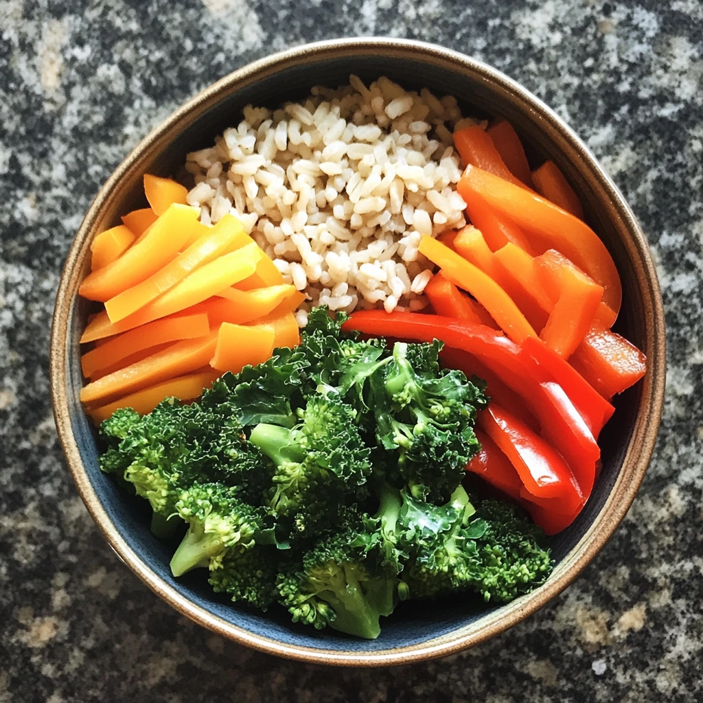 A nourishing brown rice bowl topped with kale, bell peppers, carrots, and broccoli, creating a colorful and healthy meal.